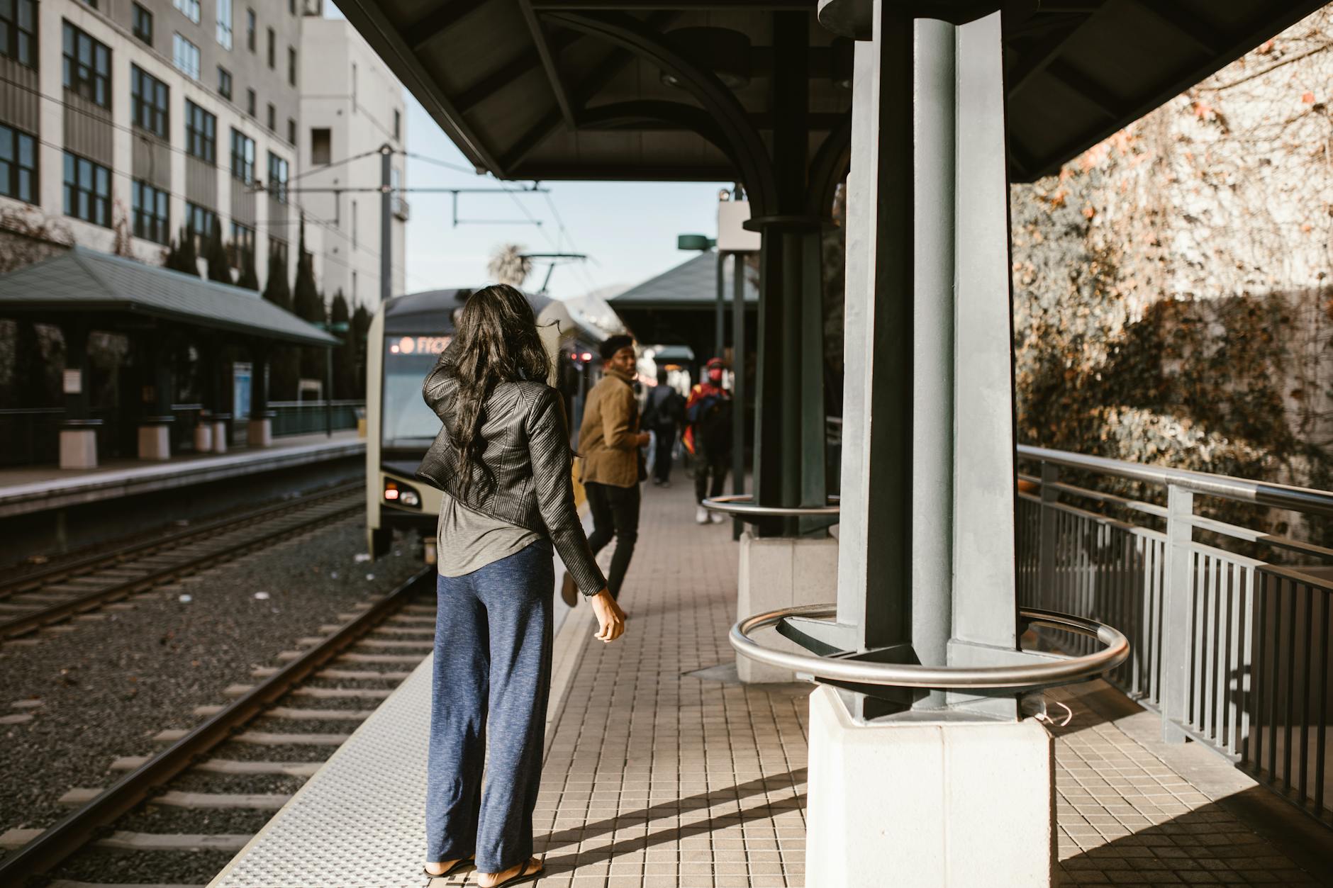 An urban train station with a woman waiting and a train approaching.